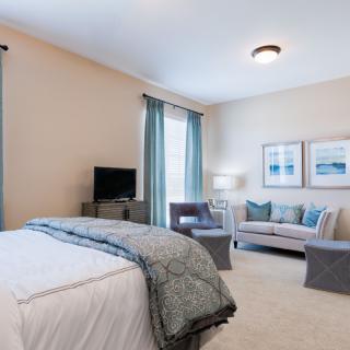A modern and cozy bedroom featuring a comfortable bed, a small sofa with decorative cushions, and tasteful artwork on the walls.