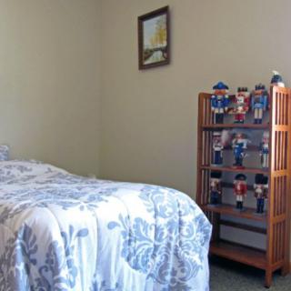 A cozy bedroom featuring a neatly made bed, a wooden shelf displaying toys, and framed artwork on the wall.