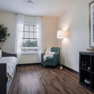 A modern minimalist bedroom featuring a cozy armchair, wooden flooring, and ample natural light.
