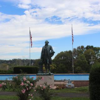 A statue standing proudly in a park, framed by flags and under a beautiful blue sky.