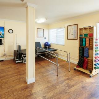A rehabilitation room equipped with exercise equipment, including parallel bars, therapy balls, and weights.