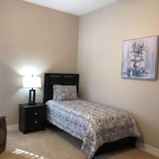 A cozy and simple bedroom featuring a single bed, nightstand with lamp, and minimalistic wall art.