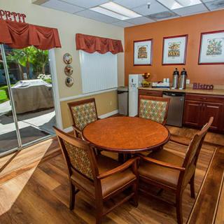 A cozy dining area with a round table, surrounded by chairs and a coffee station in a brightly lit room.