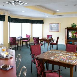 A cozy dining room with tables and chairs, featuring a puzzle on the table and large windows letting in natural light.