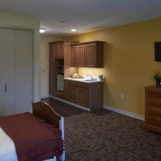 A hotel room featuring a cozy bedroom and a small kitchenette area.