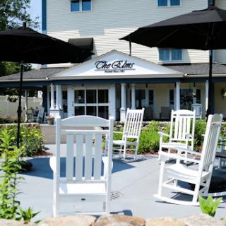 A cozy outdoor seating area featuring white rocking chairs and umbrellas, perfect for relaxation at a restaurant.