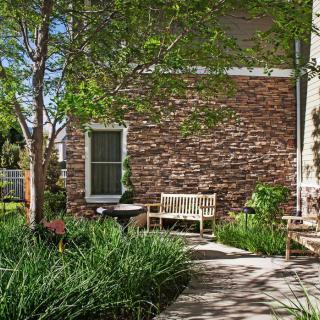 A serene garden area with a wooden bench against a red brick wall, surrounded by lush greenery.
