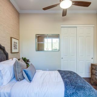 A cozy bedroom interior with a neatly made bed, decorative pillows, a ceiling fan, and a closet.