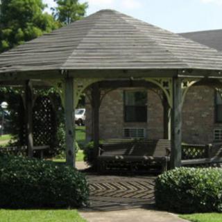 A wooden gazebo situated in a garden area with greenery surrounding it.
