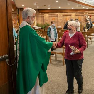 A priest greets an elderly woman after a church service, highlighting community and fellowship.
