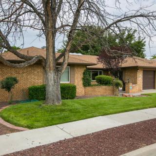 A single-story brick house with a neatly maintained yard and tree, bordered by a sidewalk.