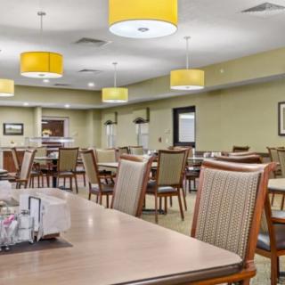 A spacious dining area with neatly arranged tables and chairs, illuminated by modern yellow pendant lights.