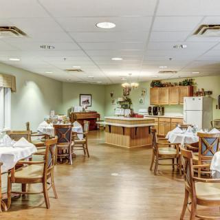 A well-organized dining room with neatly arranged tables and chairs, featuring a kitchen area in the background.