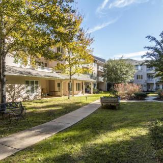 A scenic view of a residential apartment complex with lush green lawns and trees on a sunny day.