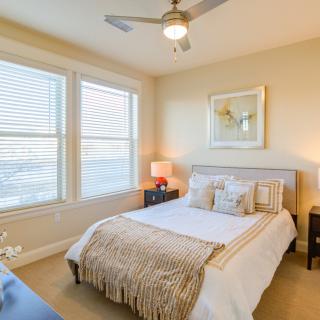 A cozy and well-decorated bedroom featuring a comfortable bed, bedside tables with lamps, and large windows allowing natural light.