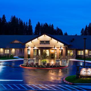 A well-lit building entrance at night, surrounded by a parking area and trees.