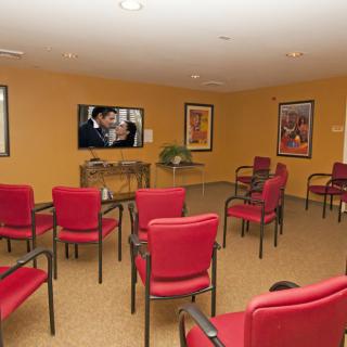A cozy meeting room with red chairs facing a television and walls adorned with artwork.
