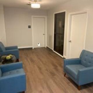 A simple waiting room with blue chairs and wooden flooring.