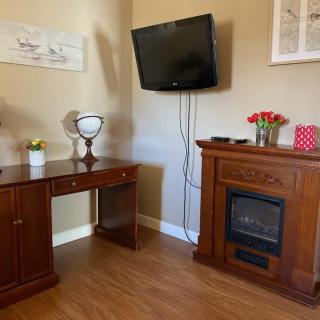 A cozy living room corner with a wooden desk, electric fireplace, and wall-mounted television.