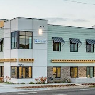 A modern commercial building featuring a blend of green and beige exterior with multiple windows.