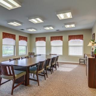 A well-lit conference room with a large meeting table surrounded by chairs and windows.