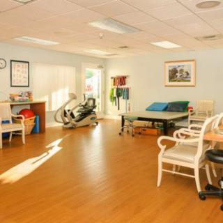 A bright and well-equipped rehabilitation therapy room featuring exercise equipment and comfortable seating.