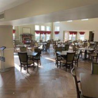 Spacious dining area with tables and chairs, illuminated by sunlight streaming through large windows.
