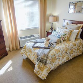 A cozy bedroom with a neatly made bed, soft lighting, and a window allowing natural light.