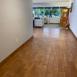 A bright and spacious hallway featuring wooden tile flooring, leading to a well-lit area with large windows.