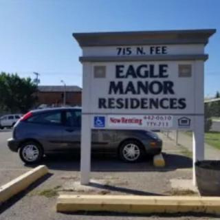 A sign for Eagle Manor Residences in a parking lot with a car parked nearby.