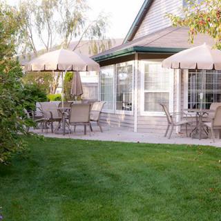 A cozy backyard patio with outdoor furniture and umbrellas, surrounded by a lush green lawn.