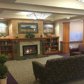 A cozy living room with a fireplace, couches, and bookshelves adorned with artwork.