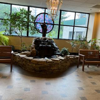 A serene indoor waiting area featuring a decorative fountain, comfortable seating, and abundant greenery.