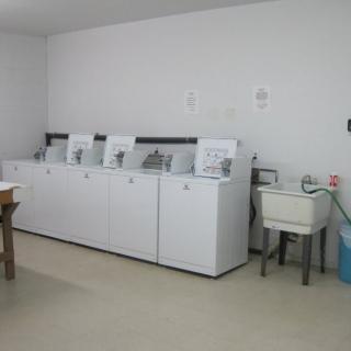 A laundry room with several washing machines lined up next to a sink.