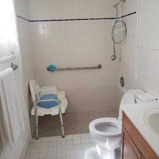 A clean and accessible bathroom including a shower, toilet, and supportive seating.