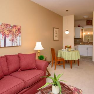 A cozy living and dining area with a red sofa, decorative wall art, and a small kitchen in the background.