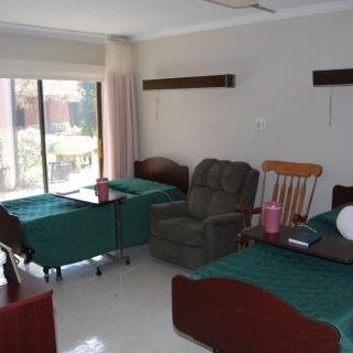 A shared nursing home or hospital room with two beds and seating area.