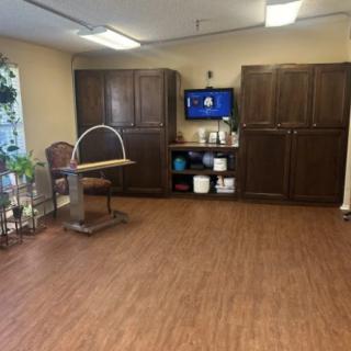 A room with wooden flooring features a chair and desk, large cabinets, and a wall-mounted television.