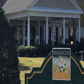 A building entrance with a prominent sign in front, surrounded by greenery.