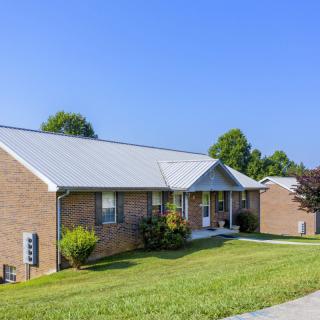 A single-story brick house with a sloping lawn and clear blue sky.