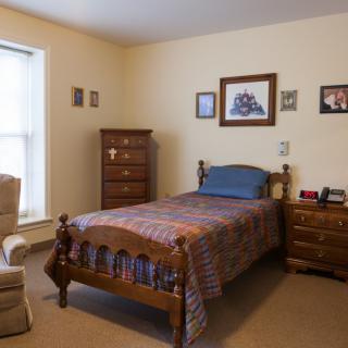 A cozy bedroom with a single wooden bed, dresser, and upholstered chair.