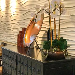An elegant interior setup with a modern wavy wall design, featuring an orchid arrangement and decorative items on a dark wooden table.