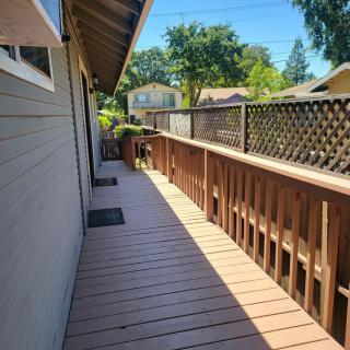 A sunny view of a wooden deck alongside a house with a fence.