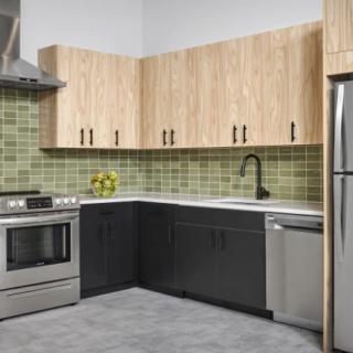 A modern kitchen featuring stainless steel appliances, wooden cabinets, and a green tile backsplash.