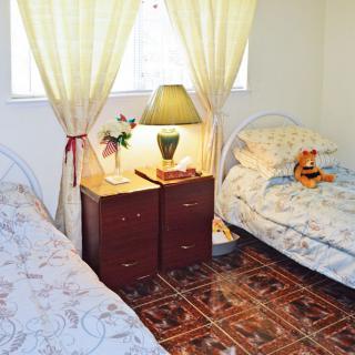 A cozy bedroom with two single beds separated by a nightstand, featuring a lamp and floral decorations.