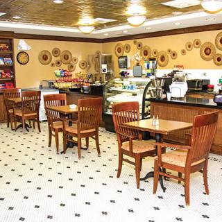 A cozy cafe interior with wooden tables and chairs, decorative plates on the wall, and a counter with coffee machines.
