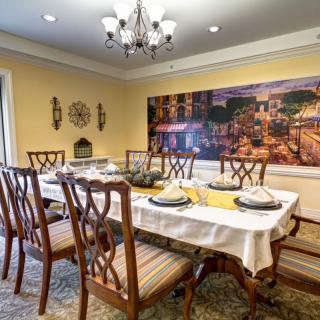 A beautifully decorated dining room with a large table and elegant chairs, featuring a chandelier and wall artwork.
