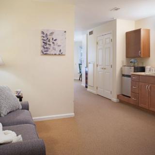 A cozy apartment interior featuring a living room with a sofa, wall art, and a small kitchenette.