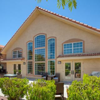 A beautiful house with large windows and a well-maintained patio area on a sunny day.