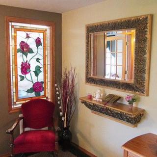 A cozy interior corner with a stained glass window, ornate mirror, and elegant red chair.